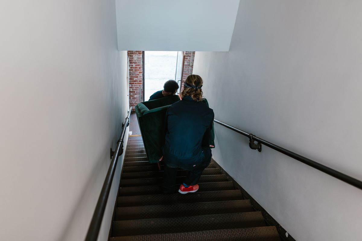 Movers carefully carrying a sofa down a narrow apartment staircase
